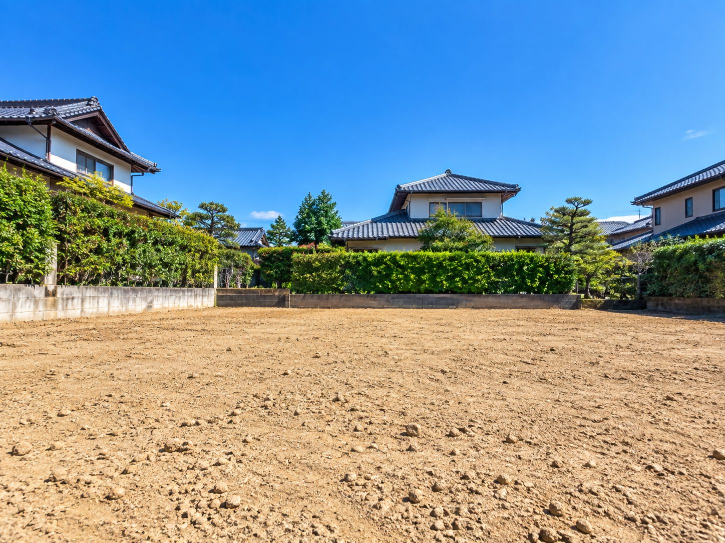 解体後、瓦屋根の家と生け垣に囲まれ、晴れた青空の下できれいにならされた更地のイメージ